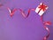 White gift box tied with red ribbon spiral on purple background.