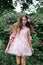 White girl 10 years old in a pink dress whirls against the background of greenery in the Park