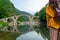 White girl backpacker looking medieval old ottoman stone structure with reflect on the water. Devil Bridge in Bulgaria with legend