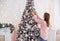 White girl in a knitted dress pink decorates a Christmas tree with Christmas toys