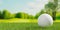 White golf ball close up on green grass or lawn with golf course fairway background, golf sports or activity concept