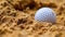 White golf ball lying in a sandy area with a detailed texture.