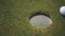 A white golf ball rolls past in holes on a golf course with green grass, close-up. Moment the ball misses and the white