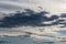 White-gray clouds in the sky illuminated by the setting sun. Light blue sky behind dark and dramatic storm clouds.