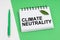 On a white-green background lies a pen, a leaf of a plant and a notepad with the inscription - climate neutrality