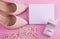 White greeting card with wavy edge. Beige leather shoes with high heel, greeting card and accessories on pink background.
