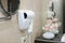 A white hairdryer is hanging on the wall in the bathroom. Photo in the interior. Flowers and the mirror are out of focus. Hotel