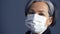 White-haired business woman in a protective mask looks at the camera standing on a dark background. Business concept
