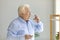 White-haired chubby senior male taking prescribed medicine with a glass of water