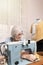 white-haired older woman sewing in front of an old sewing machine in a house room