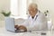 White-haired senior doctor typing on laptop keyboard sitting at desk in hospital office