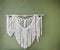 White handmade macrame decoration hanging on green wall, bohemian style decorative item