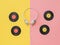 White headphones on the border of pink and yellow background and four vinyl discs.