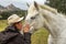 White horse in the green meadow receiving cuddles from his cowgirl with the white cowboy hat with many hugs and caresses and kisse