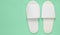 White hotel slippers on a mint blue pastel background, top view, minimalist trend.