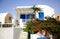 A white house with blue painted doors and window frames and bush with flowers on the front scene in Santorini Island