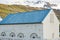 White house with blue roof in small town Seydisfjordur on East Iceland in summer with mountains and snow