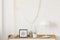 White industrial lamp, photo in frame and plant in pot on wooden console table in elegant living room with white wall