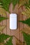 White IQOS battery lies on decorative abstract wooden texture with green and yellow leaves of fern