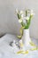 White Iris flowers bouquet in vase, decorative eggs, ceramic bunny on white table near white wall.