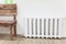 White iron radiator of central heating near wooden bench in room