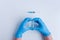 On white isolated background, the doctors hands in medical blue gloves depict heart shape gesture