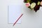 A white jotter and a red pencil next to peonies