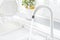 White kitchen faucet running with blurred windowsill and dish dryer