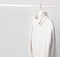 White knitted wool sweater on a white wooden hanger against the background of the light wall. Autumn and winter clothes. Store con