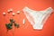 White lace panties with tampon on a coral background. Female underwear for the bride with delicate flowers on an orange background