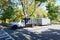 A white landscaping truck with a long white enclosed trailer trailer seen on a shady residential asphalt street