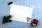 a white leaf on a blue surface framed by a Santa Claus hat with green fir twigs, gift boxes and snowflakes - sweets