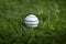 White leather Cricket ball resting on a green grass cricket ground pitch