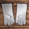 White leather welder gloves on a wooden background. A studio photo with hard lighting