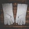 White leather welder gloves on a wooden background. A studio photo with hard lighting