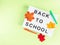 White lightbox with back to school text on green background with autumn leaves and pens