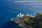 White lighthouse is on the top of the hill in Ligurian Sea with the sailing white motor boat on the background. Arial view on the