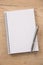 White lined notepad with a metal ring wire binding and a silver pen opened on a wooden surface