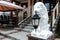 White lion statue holding an old lantern in front of a hotel or restaurant facade. Stairs in the background. Hospitality concept.