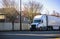 White long haul big rig semi truck transporting commercial cargo in dry van semi trailer running on the city street