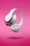 White luxury music portable headphones in the air on neon pink background. Trendy magic flying levitation close up