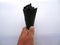 A white man holds a black nibbled ice cream in a black waffle cone with a white paper napkin on a cloudy summer day