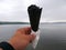 A white man holds a black nibbled ice cream in a black waffle cone with a white paper napkin on a cloudy summer day