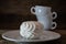 White marshmallows in a white plate, on a wooden table against the background of a pyramid of coffee cups.