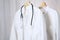 White medical doctor or physician lab coats with stethoscope hanging on clothes hangers, copy space