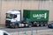 White Mercedes Actros truck loading a green container trailer along Barcelona's Ronda Litoral