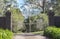 White metal driveway entrance gates set in brick fence leading to rural property with eucalyptus trees in background