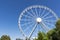 White metal Ferris wheel with cabins on background of blue sky,