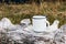 White metal mug sitting on old wood log. Blurred grass, meadow background. Outdoor tea, coffee time. Mockup of enamel