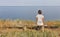 White middle aged woman sitting on wooden bench with seascape